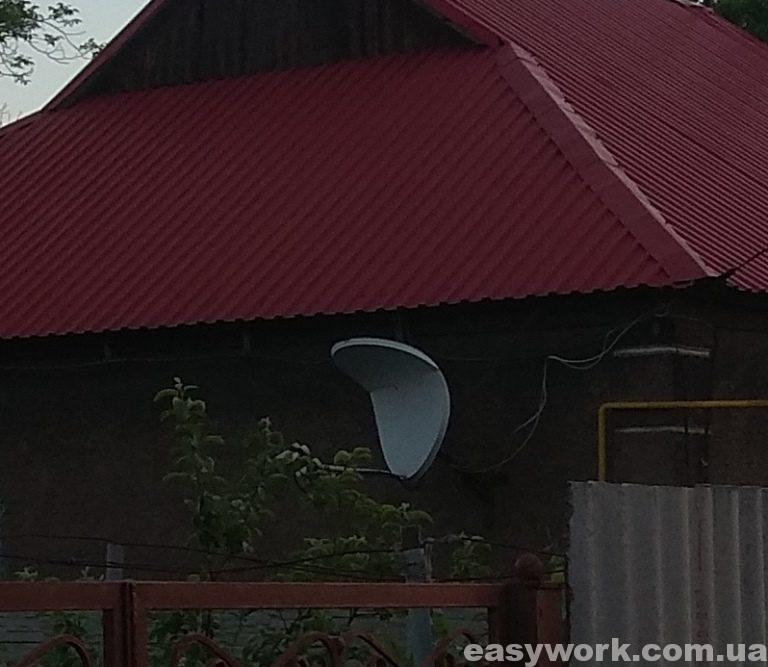 Погнутая спутниковая тарелка от съехавшего снега с крыши
